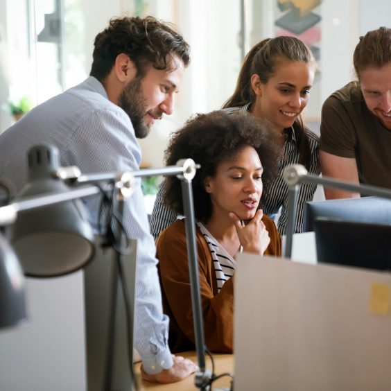 Diverse group of professionals meeting in office. IT programmers use computer, talk strategy